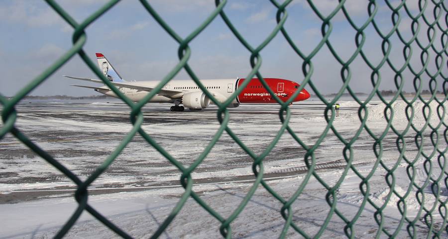 An airplane fly over the chain link fence enclosure in the airport.