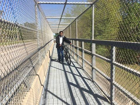 A pedestrian passage with three sides chain link mesh next to the highway.
