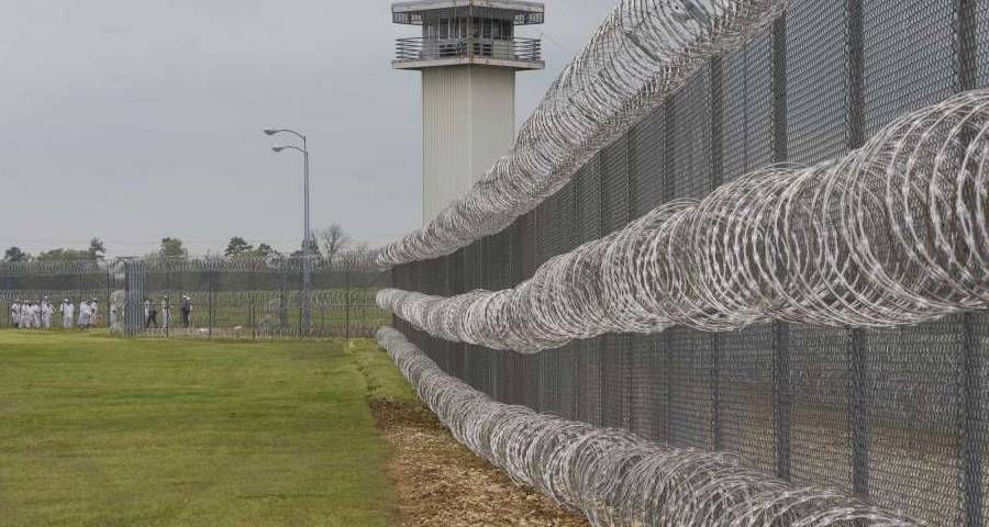 A tall prison fence with concertina razor wires at the top.