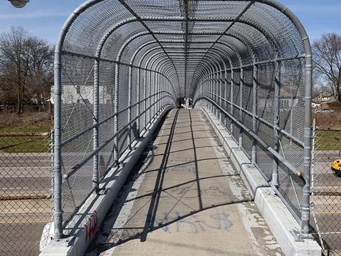 A pedestrian passage with three aspect of chain link fence cross over highway.