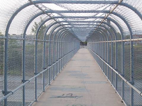 A aerial pedestrian passage with concrete ground and strong sturdy chain link railing and roof.