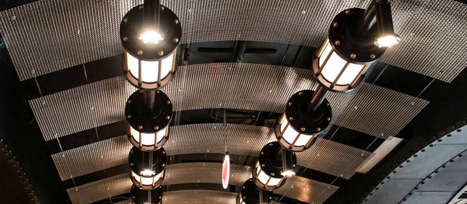 Arch shaped woven mesh ceiling hung overhead of a room, two rows of lamps hung below the woven mesh ceiling.