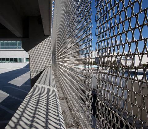 A pedestrian walkway with stainless steel spiral mesh facade is next to a river.