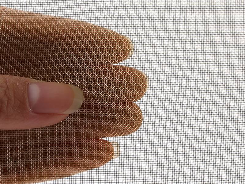 A roll of brass insect screen and a section of the screen hold by a hand.