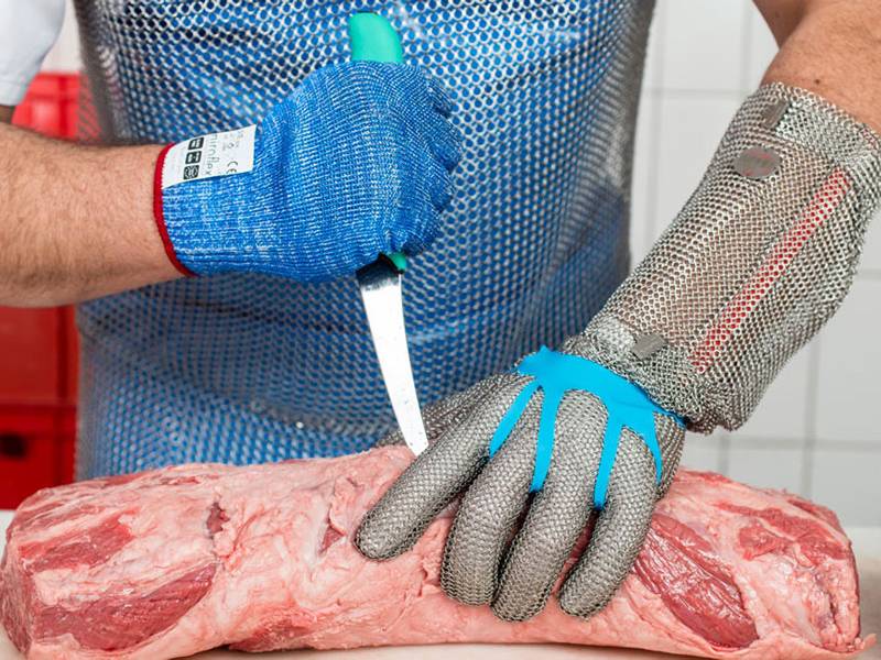 A man wearing chainmail gloves when his cutting the meat.