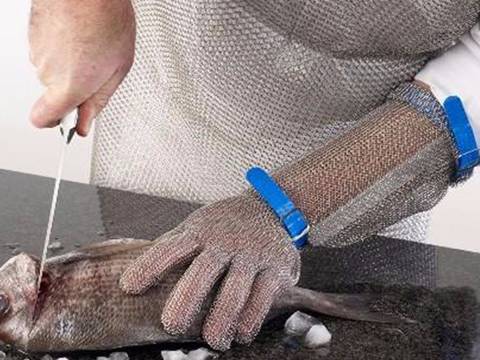 A man is wearing long-cuff chainmail gloves when cutting fish.