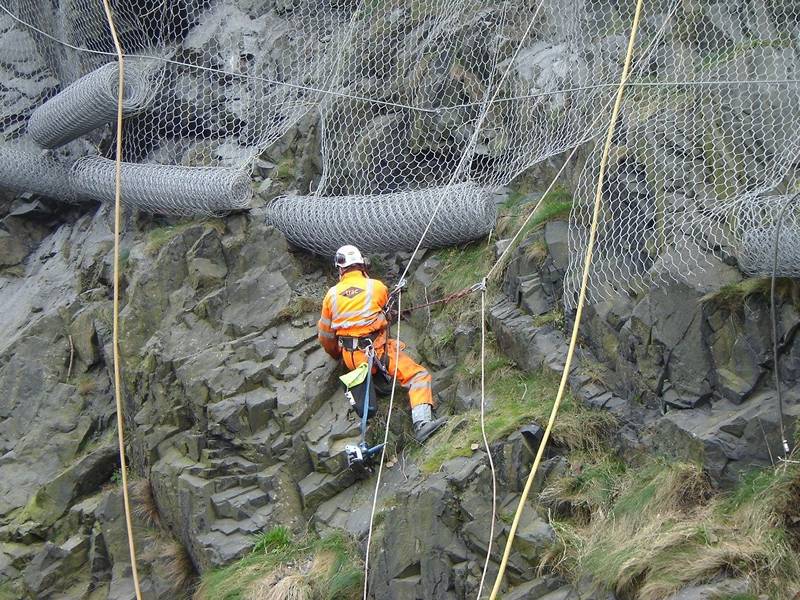 A worker is installing the hexagonal wire mesh for rockfall barrier.