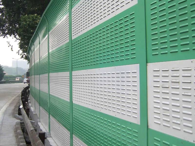Green and white aluminum sound barriers with louver holes installed along a heavy freeway.