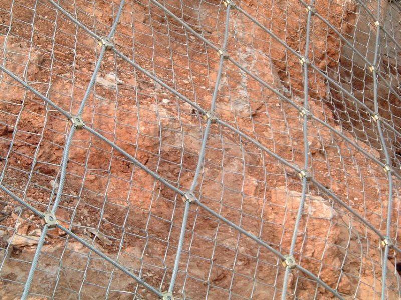 Steel wire rope net with chain link fence as an active rockfall barrier installed on the soil surface.