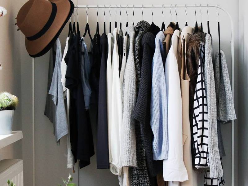 Black foam hangers hang various kinds of clothes on a metal stick. 