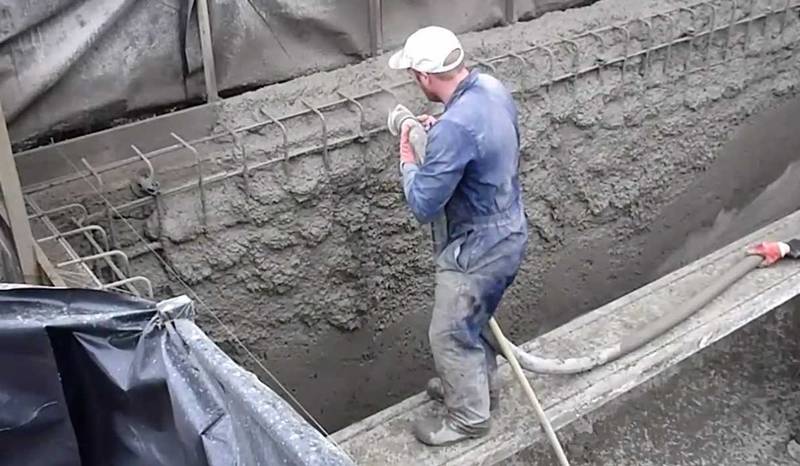 A man holding a soft pipe and spraying concrete to the wall.